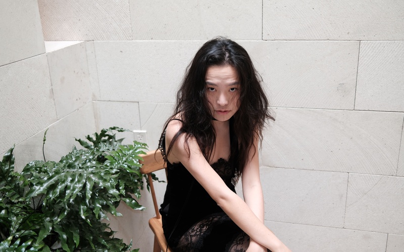 A portrait photo of a person in front of a concrete wall with a plant.