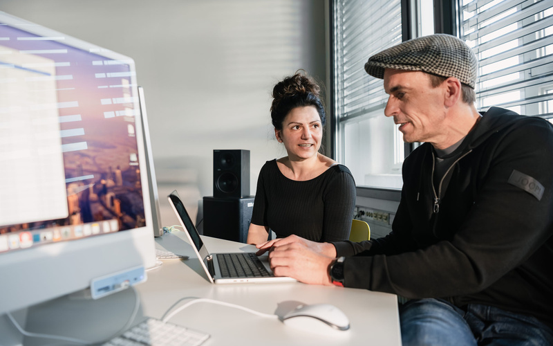 Zu sehen ist sind zwei Personen, die vor einem Laptop sitzen. 