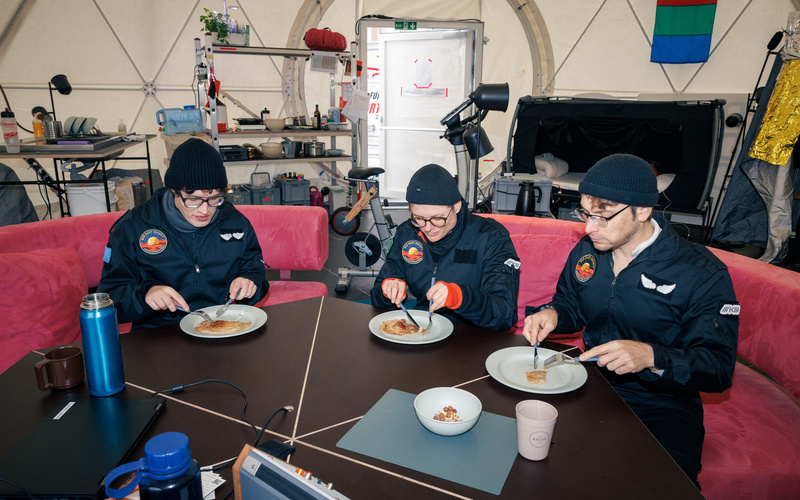 Zu sehen sind drei Personen, die gemeinsam an einem Tisch sitzen und essen.