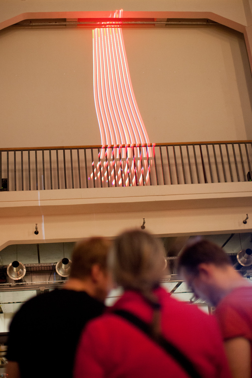 Drei Menschen blicken auf Lichtstrahlen, die an die Wand projeziert sind
