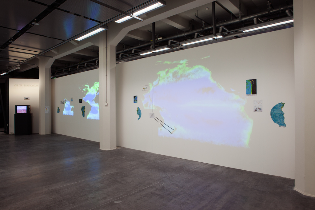 Kartenwerk Fragmente auf einer weißen Wand, darauf Projektionen geografischer Bilder.