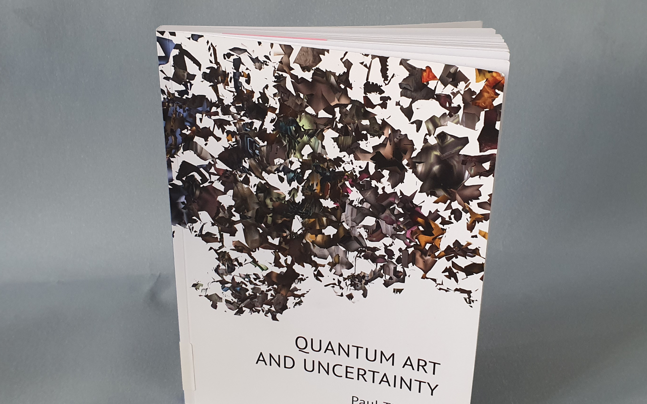 zu sehen ist das buch »quantum art and uncertatinty« von paul thomas, stehend, leicht aufgeschlagen, vor blau-grauem grund.
