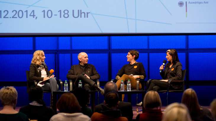 Four people are sitting on a stage while talking