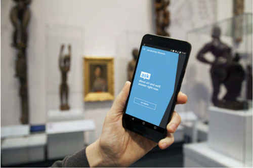 Mobiltelefon in der Hand eines Museumsbesuchers. Auf dem Bildschirm wird der Museumsbot ASK gestartet.