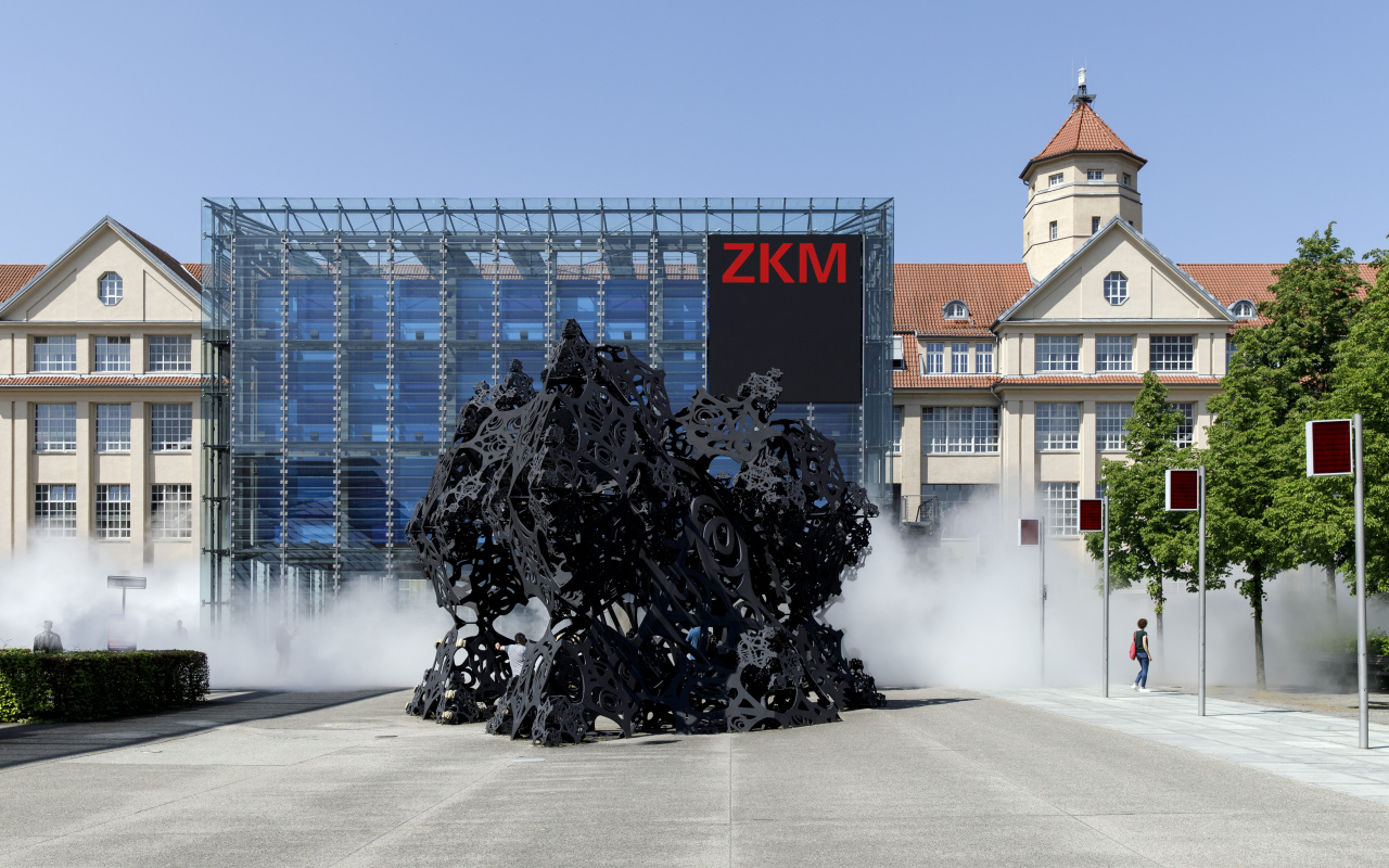 The photo shows the entrance of the ZKM as well as the cube surrounded by a light fog.
