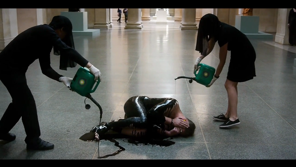 Two people are spilling oil over a person lying on the floor