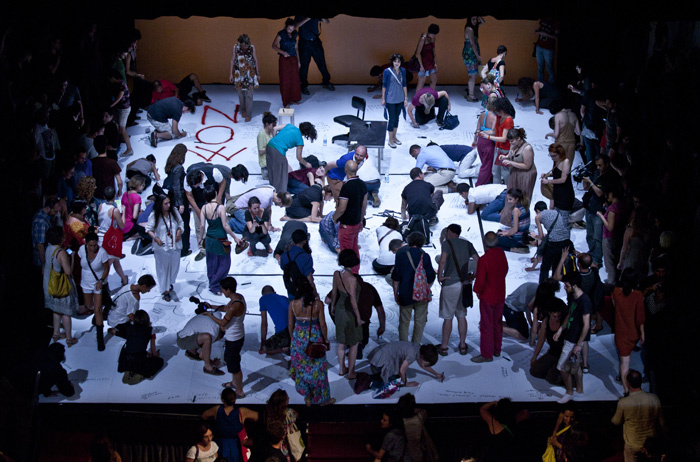 A lot of people are standing an stitting on a stage and are painting