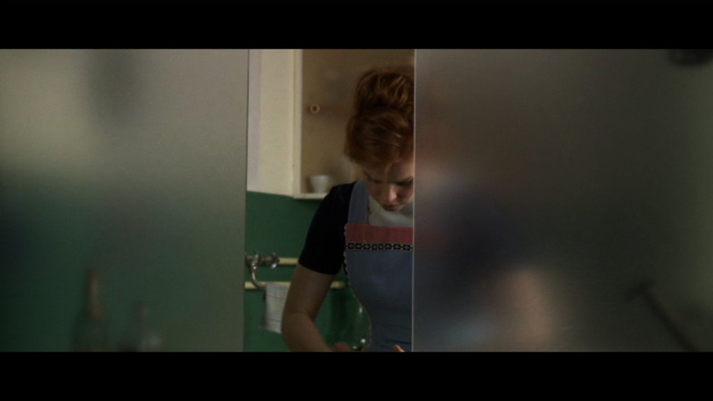 A Woman in the kitchen behind of a glass panel