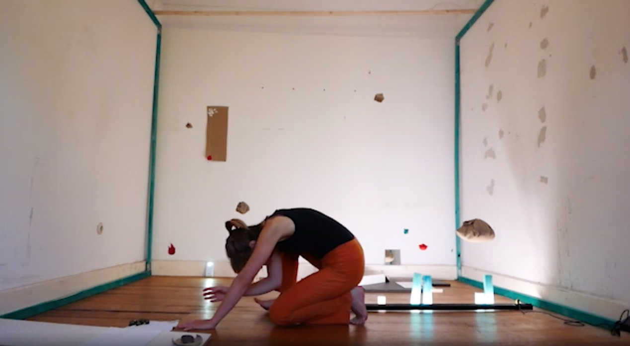 The image shows a person kneeling in a room full of objects.