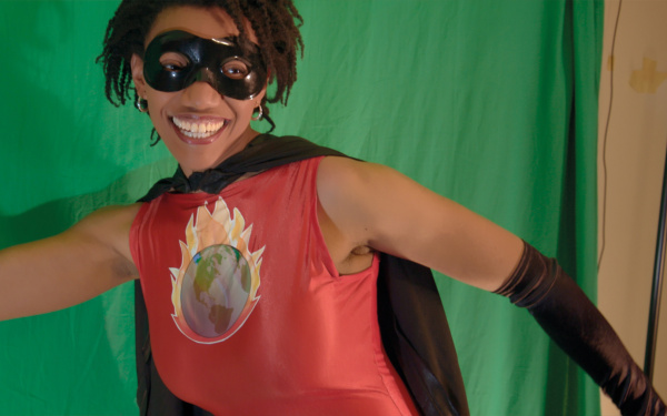 A woman is wearing a superhero costume, smiles and raises her right fist