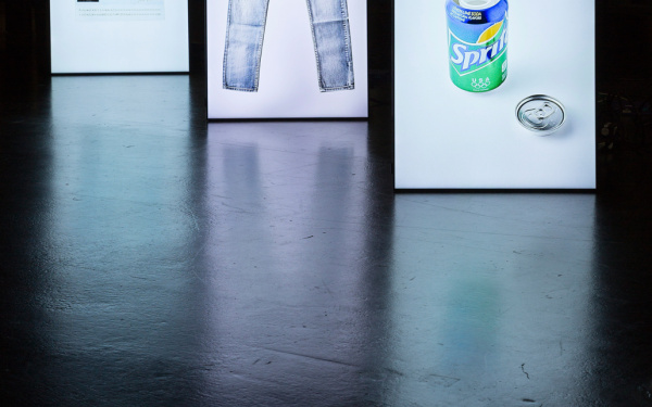 Drei hintereinander stehende Leuchtständer, auf denen eine Hose, eine Sprite-Dose und ein Ausweis zu sehen sind