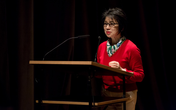 A woman in a red pullover talks to the audience
