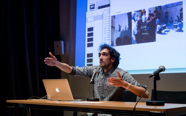 A man speaks to the audience wildly gesticulating