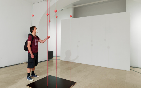 Ein Mann fasst ein Kunstwerk der Ausstellung »Is it working?« an, das aus Schnüren besteht, die zwischen der Decke und dem Boden gespannt sind.
