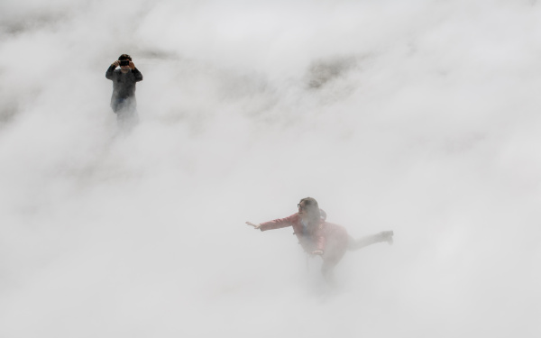 Zu sehen ist eine auf einem Bein balancierende Frau mit ausgestreckten Armen, halb versteckt im Nebel.