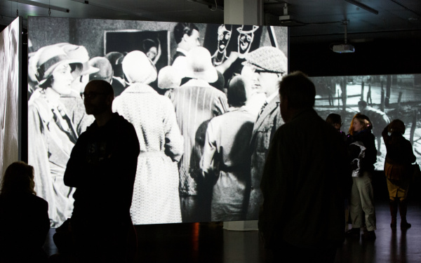 Das Foto zeigt den Ausstellungraum mit einer großen Projektion eines schwarz weiß Filmes.