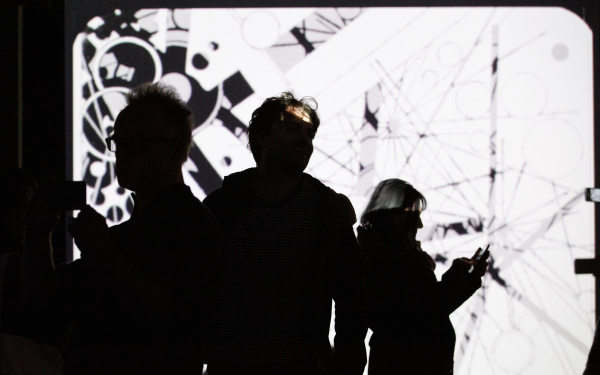 Foto von Menschen vor einer Leinwand mit einem abstrakten Video in Schwarz-Weiß – Eine Impression der Ausstellung »bauhaus.film.expanded« am ZKM Karlsruhe.