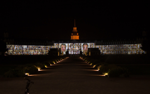 Die Fassade des Karlsruher Schlosses bespielt mit vielen Passbildern verschiedener Personen.