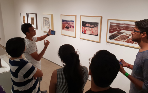 Eine Gruppe junger Menschen betrachtet an der Wand hängende Kunst. 