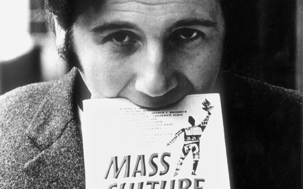 Die Portraitaufnahme zeigt Peter Weibel im Rahmen der Ausstellung »respektive Peter Weibel«. Auf dem Foto trägt der Künstler ein Buch mit seinem Mund.