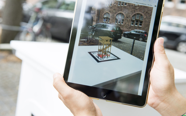 Auf einem Tablet-Bildschirm ist eine virtuelle Skulptur zu sehen, den realen Raum eingebettet ist.