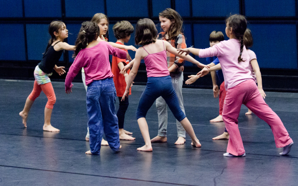 Eine Gruppe von Kindern bei einem Tanzworkshop stehen in einer lockeren Kreisformation.