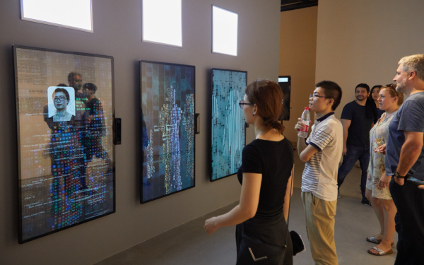 A woman stands in front of the artwork YOU:R:CODE that consists of large screens