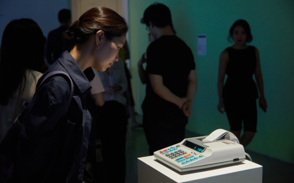 Photo of the exhibition "Open Codes. Connected Bots". An old pocket calculator with a thermal paper roll calculates to generate bitcoins.