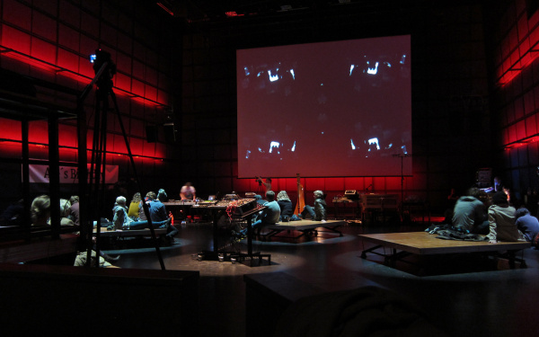 Unbestuhltes ZKM Medientheater mit Menschen, die auf dem Boden sitzen