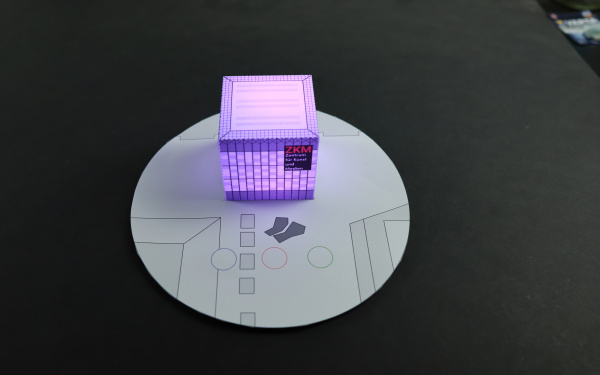 Eine Miniatur des ZKM Kubus zum Selberbasteln, der lila leuchtet.