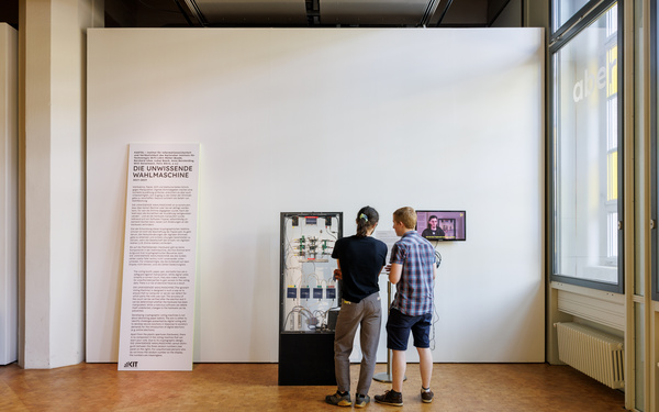 Zwei Personen stehen vor der "Unwissenden Wahlmaschine", eine interaktive Installation