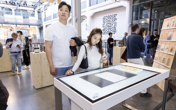 Zu sehen sind zwei Personen, die in einem Ausstellungsraum vor einem Leuchttisch stehen.