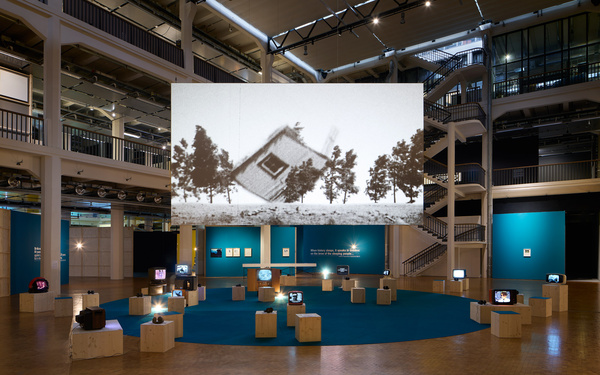 Zu sehen ist ein Ausstellungsraum mit einer großen Leinwand.