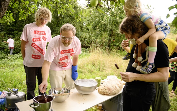Auf dem Foto sind Personen zu sehen, die T-Shirts mit der Aufschrift „School of Fire“ tragen. 