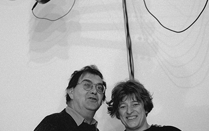 S/W Fotografie. Über zwei Personen hängt eine E-Gitarre.