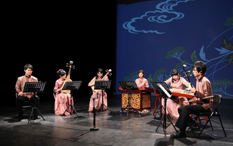 Six musicians in traditional Chinese clothing with their instruments on stage