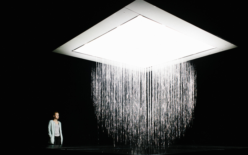 Aufnahme der Installation 3D WATERMATRIX, die Wasser formgebend von der Decke zum Boden fallen lässt. Eine Person betrachtet die Installation. 