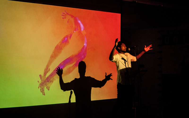Artist on stage, his shadow appears behind him on a canvas.