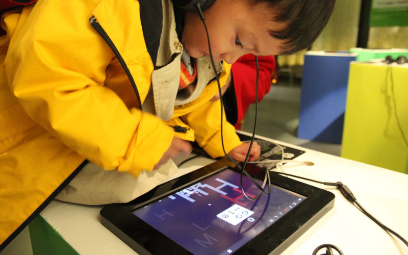 Ein kleiner chinesischer Junge ist über ein Ipad gebeugt. 