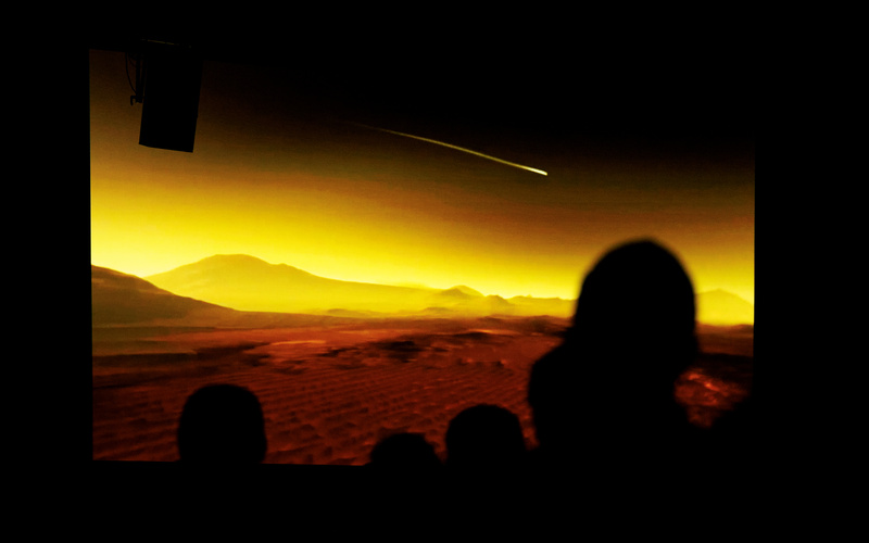 Zu sehen ist eine weite Landschaft mit Silhouetten im Vordergrund.