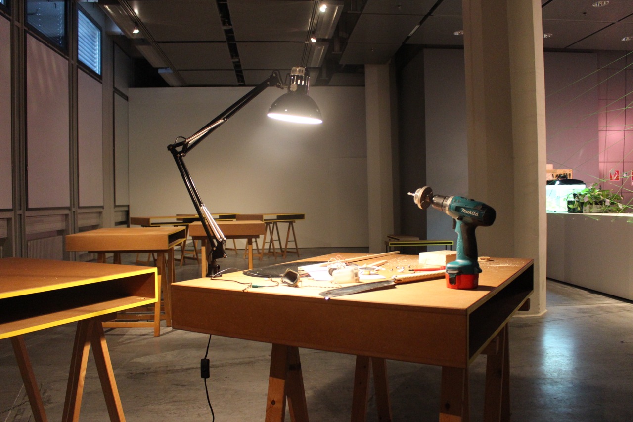 A wooden table on which a lamp and a drill stands