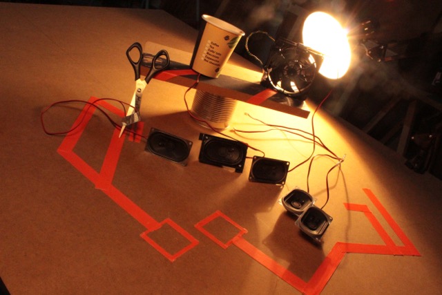 Various speaker boxes are illuminated by a desk lamp.