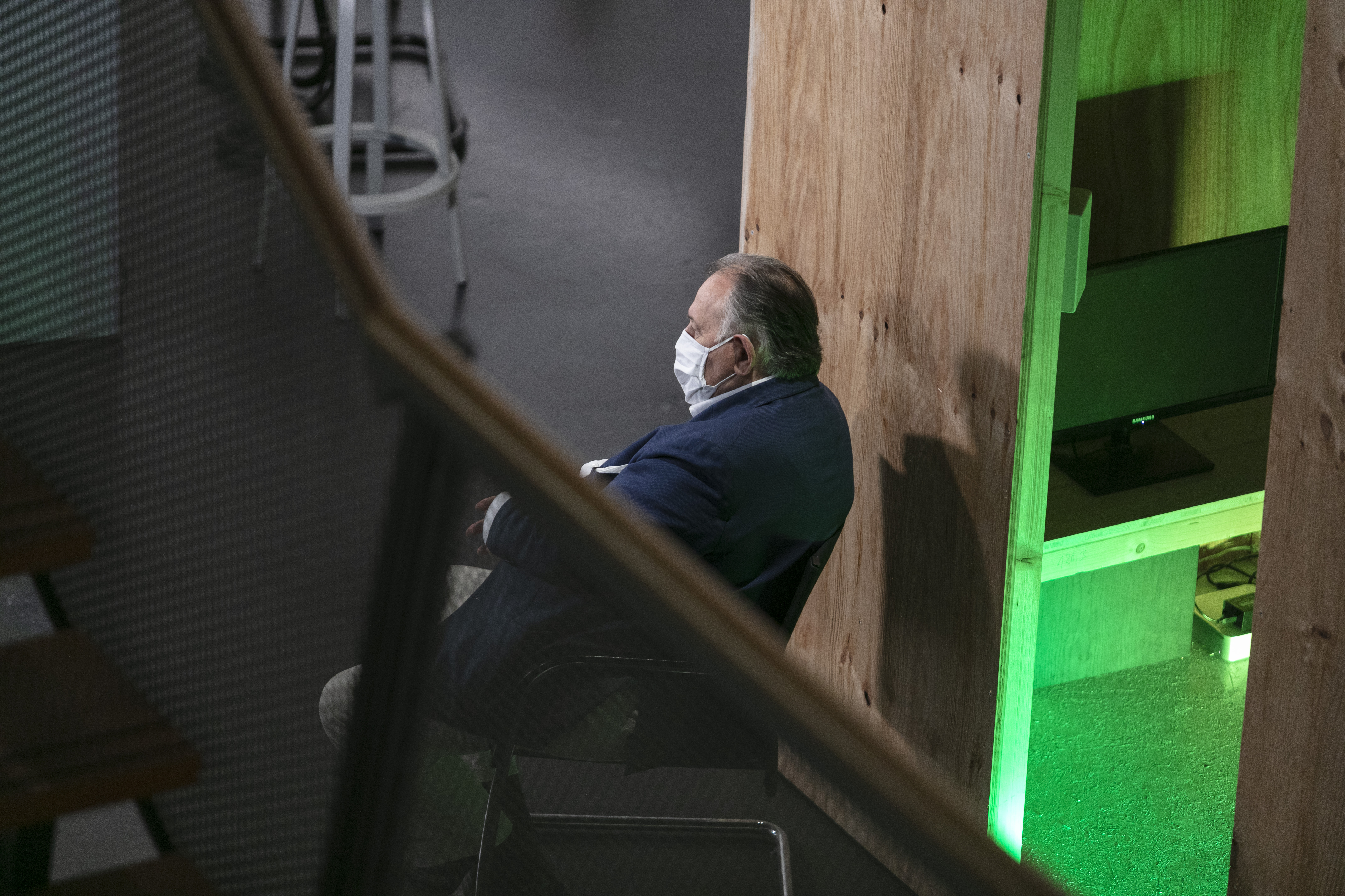 Peter Weibel sitzt mit einer Mund-Nasen-Schutz-Maske auf einem Stuhl und schaut aus dem Bild raus.