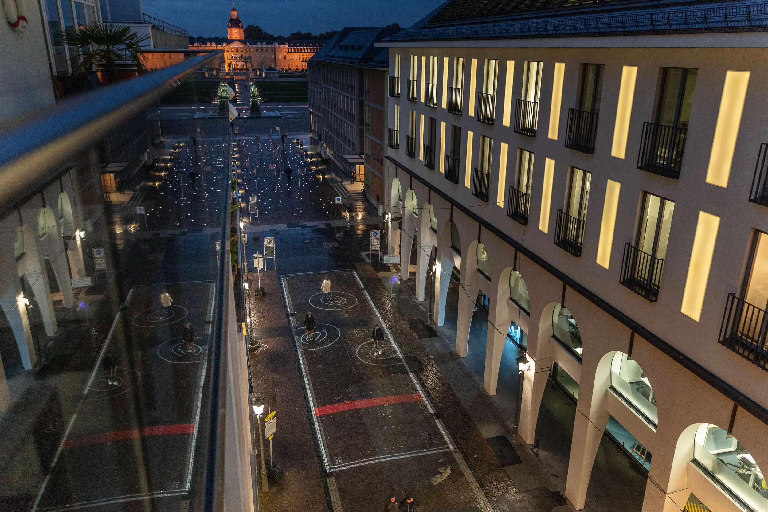 Zu sehen ist die Ansicht einer Straße von oben. Auf dem Boden sind  spiralförmige Kreise aus Licht. Im Hintergrund ist das Karlsruher Schloss erkennbar. 