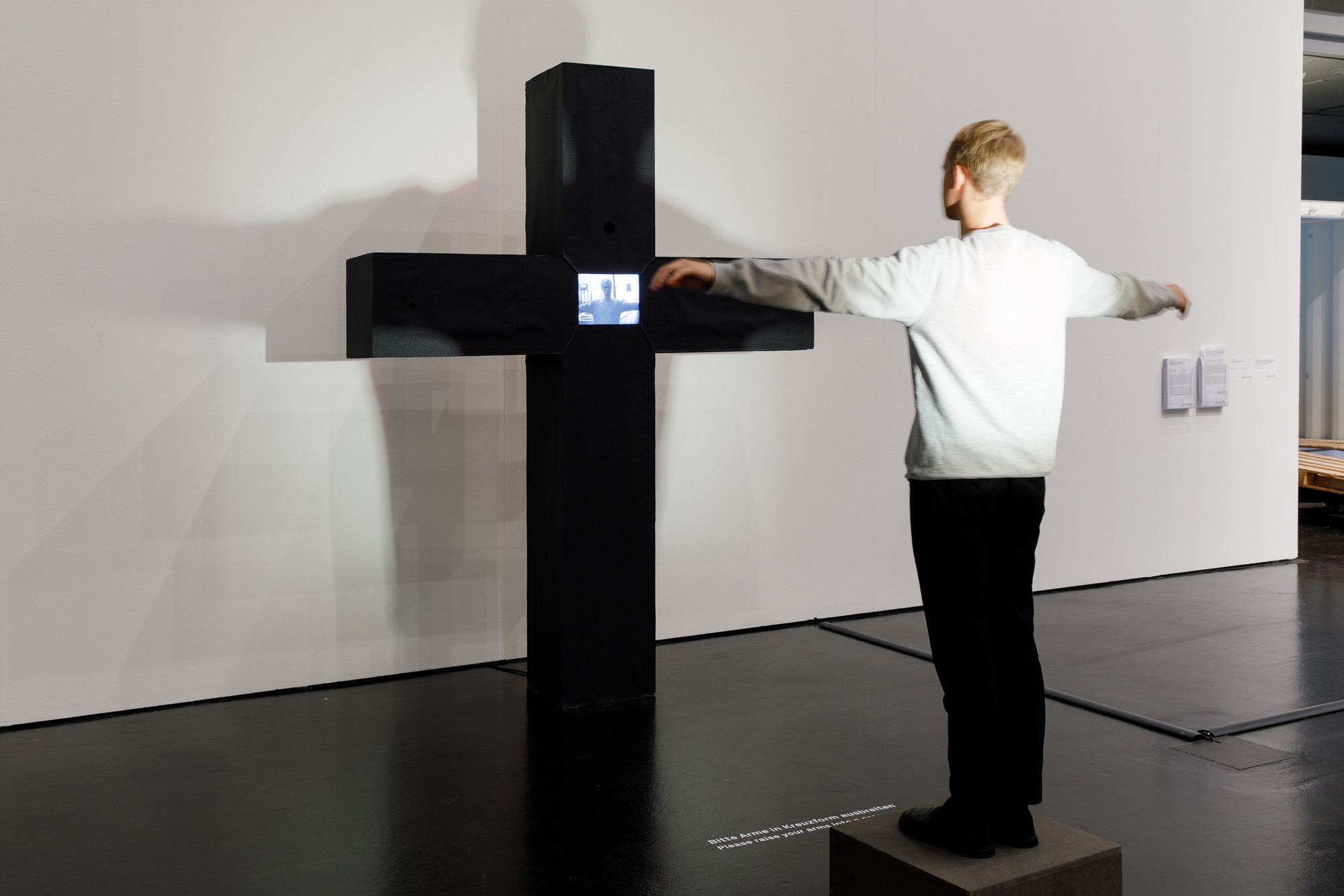 Peter Weibel's interactive video culture: A massive black cross. Where the struts of the cross meet is a monitor. On the monitor you can see the person standing in front of the cross, stretching out his arms as if he himself was hanging there.