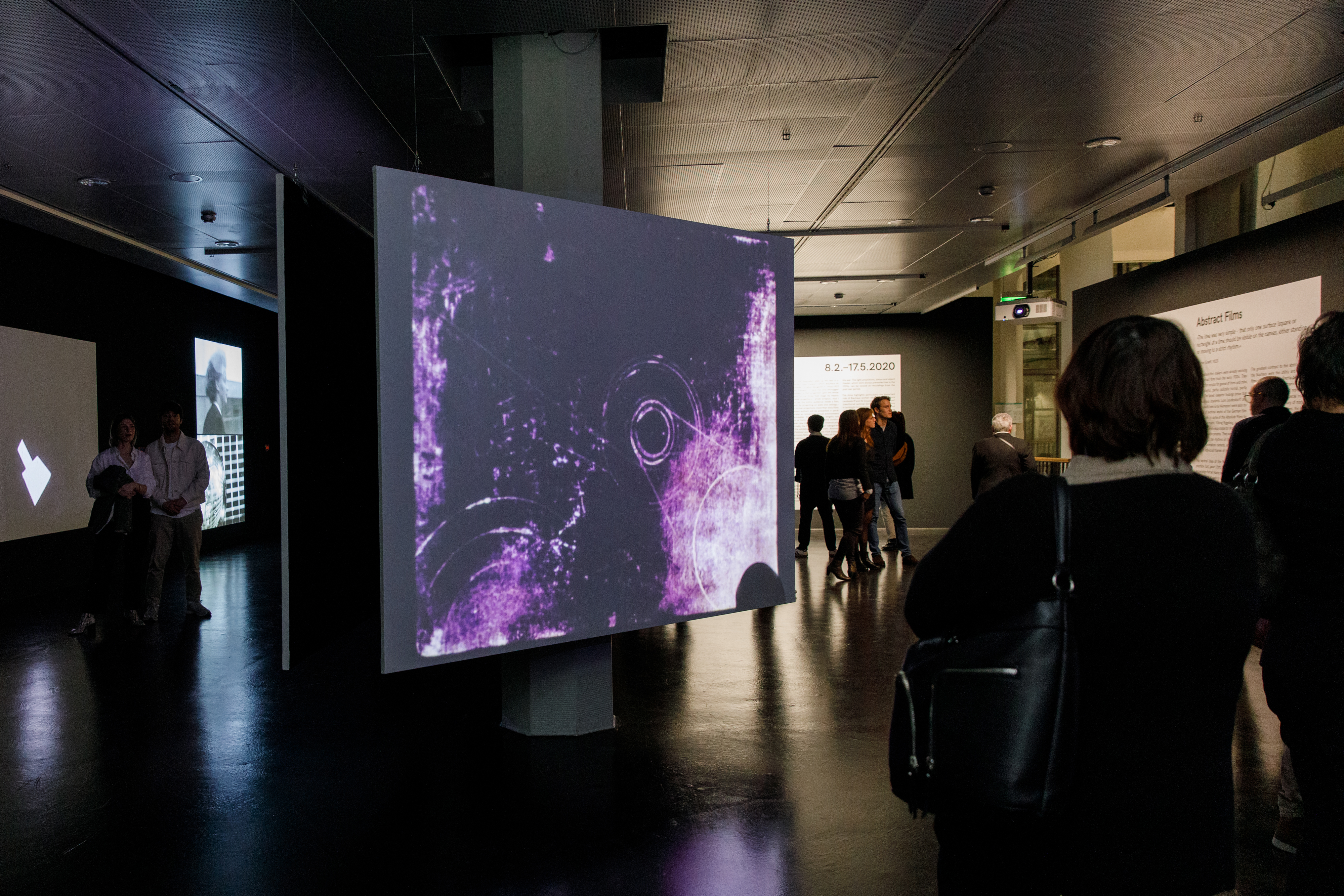 Photo of people in front of a projection screen with an abstract video in purple - an impression of the exhibition »bauhaus.film.expanded« at the ZKM Karlsruhe.