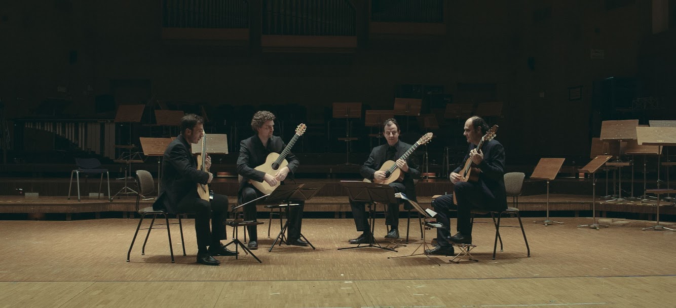 Four men are sitting in an open circle with guitars in their hands.