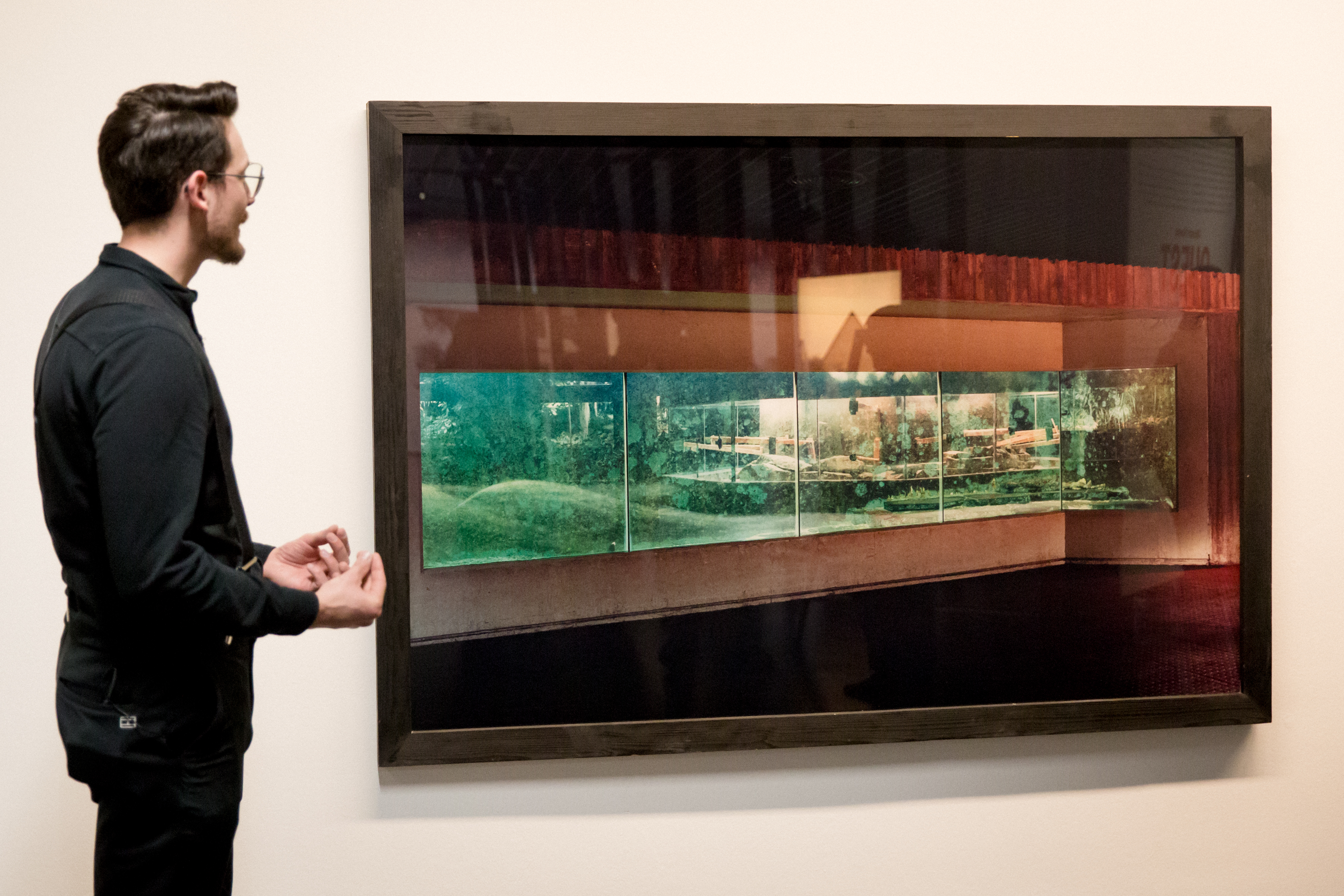 A speaking man stands in front of a large photography