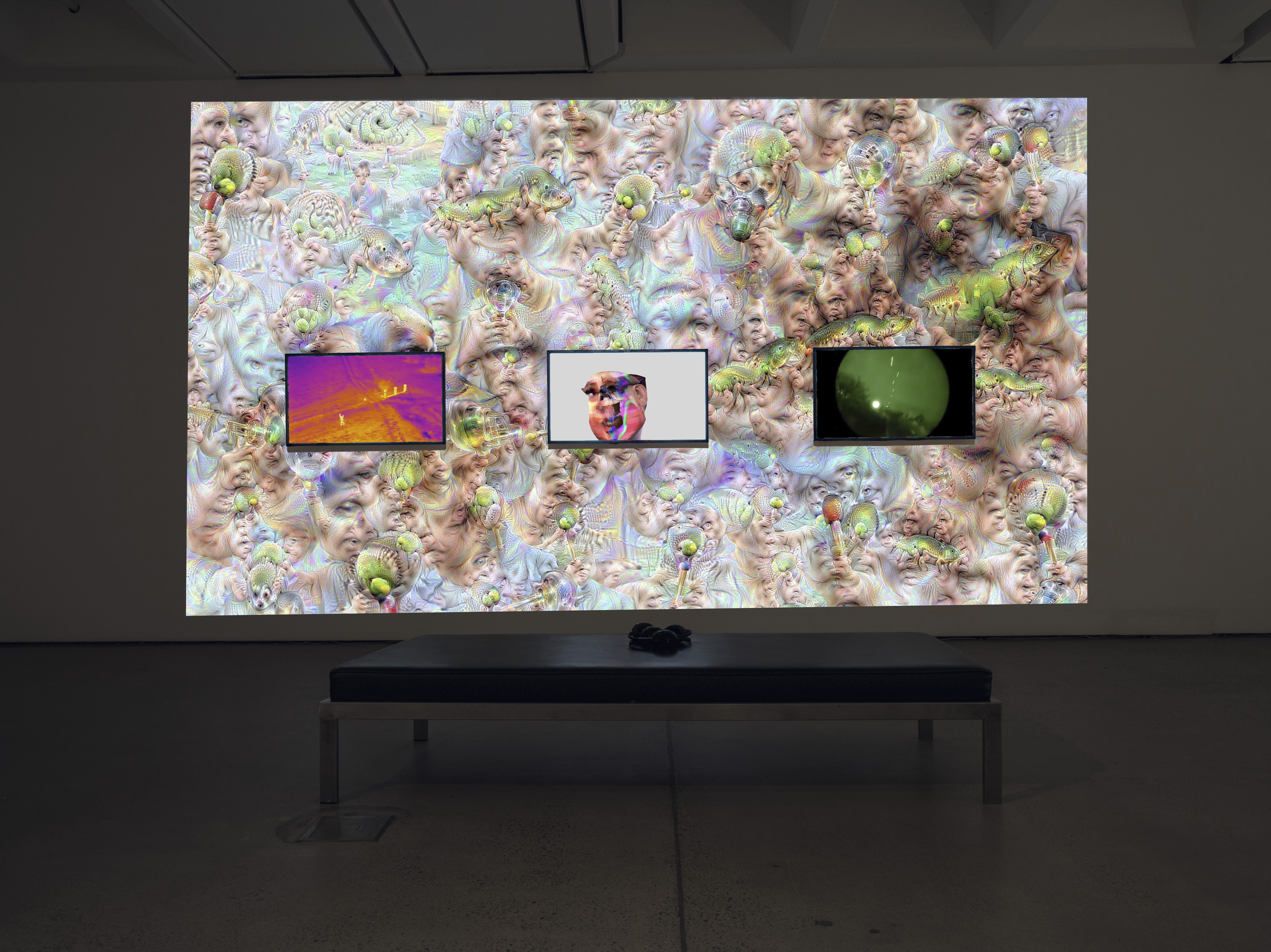 The photo shows an exhibition view of the work »im here to learn so :))))))«. Shown is a large screen in the background and three screens in the foreground. They show psychedelic cosmos and the chatbot Tay.