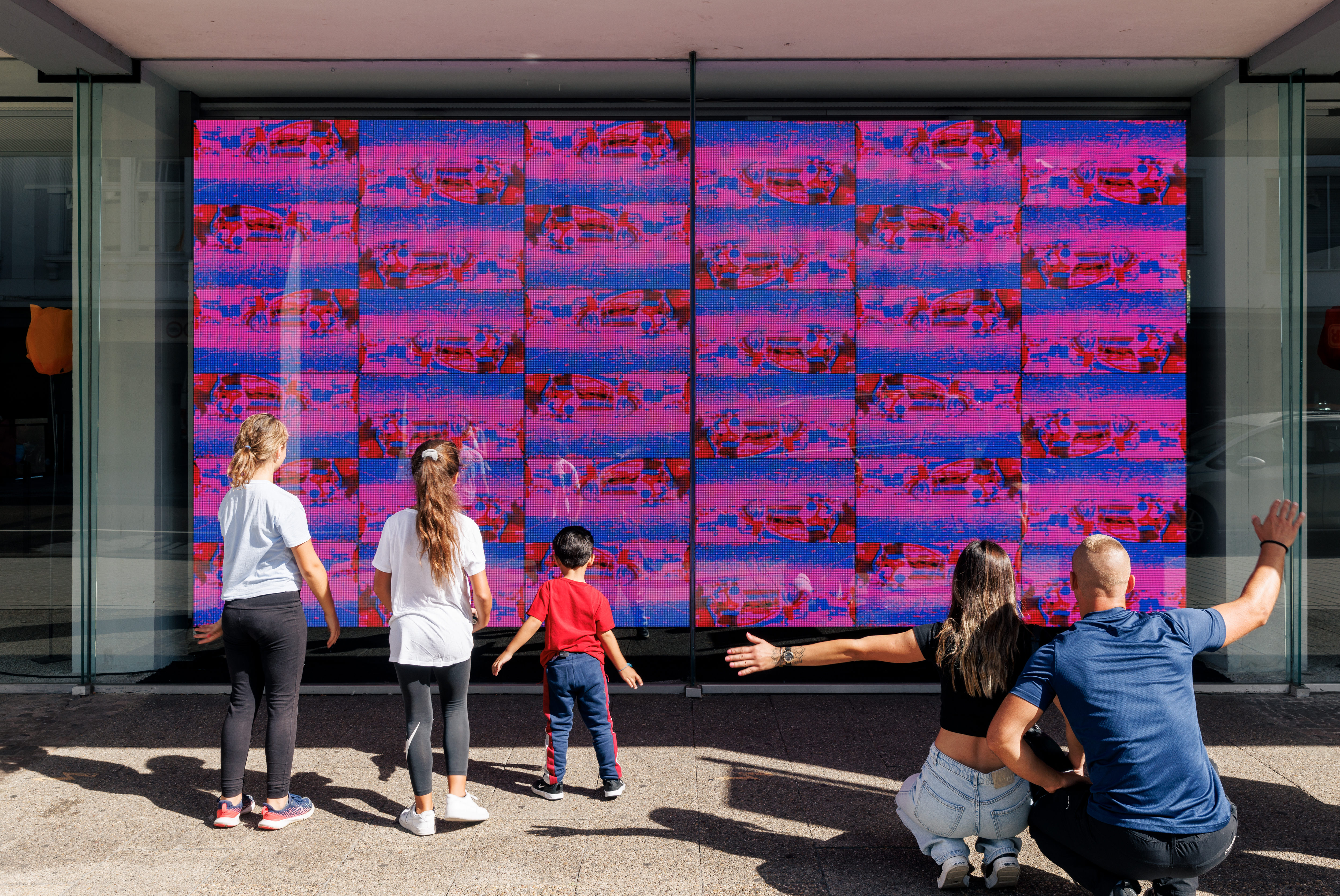 Auf dem Bild sieht man die Videoinstallation »footprint« von Jonas Denzel. Auf einem großen Screen sind lauter kleiner Bilder die von den Beinen von Passanten aufgenommen wurden. Eine fünfköpfige Familie steht davor und interagiert mit dem Kunstwerk.